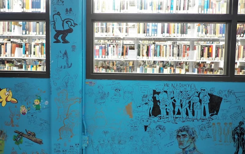 Spatial workshop 1 – Image of the student art wall – This wall feels full of energy and interaction. The bright blue color catches attention. The drawings made by different students show a mix of chaos, expressing creativity in many voices. The wall also works as a visual transition. The colourful and busy surface leads the eyes through the window into the quiet and organized library inside.